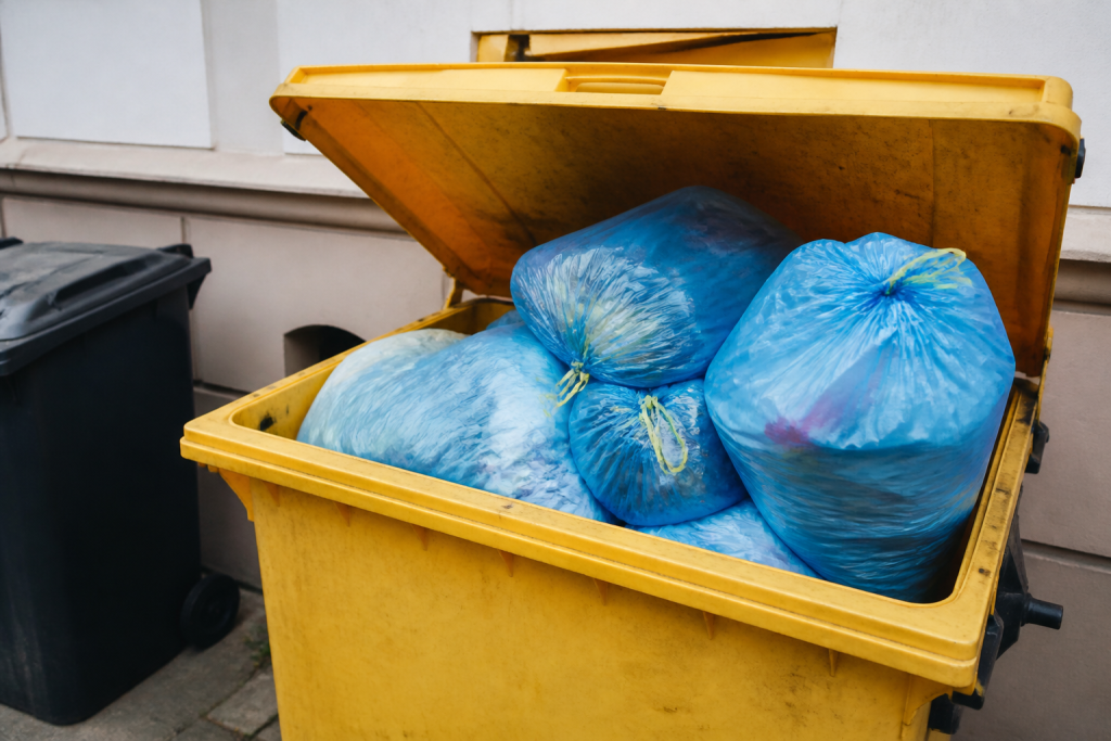 Conteneur jaune ouvert rempli de sacs bleus